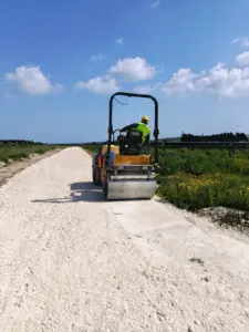 Rullo compattatore in azione su sottofondo stradale bianco in calcarenite per impianto fotovoltaico